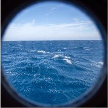 Der Blick aus einem runden Schiffsfenster aufs offene Mittelmeer: Es ist nur bewegtes Wasser und Himmel zu sehen. 
